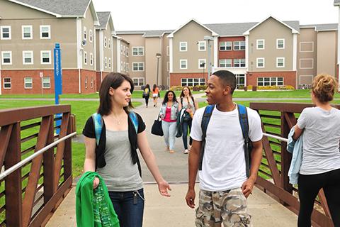 Students walking across the pedestrian bridge between the residence halls and the campus